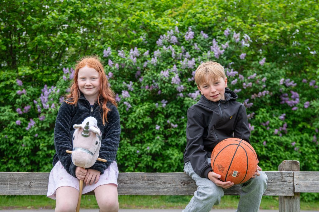 Bild på en tjej som håller i en käpphäst och en kille som håller en basketboll. Båda två sitter på ett staket.