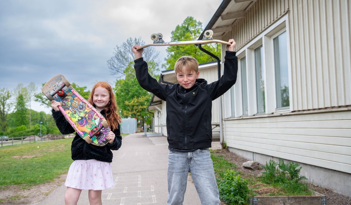 En tjej och en kille håller var sin skateboard. Killen håller sin ovanför huvudet.